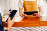Crop anonymous female colleagues surfing internet on cellphone with black screen and tablet in cafe