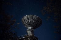 From below of blue starry sky over radio telescope and trees with leaves