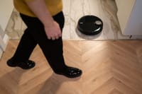 A robotic vacuum cleaner operating on a wooden floor, viewed in high angle indoor setting.