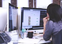 Professional woman focused on work using dual monitors in a modern office.