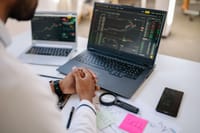 Business professional analyzing stock market data on dual laptops in an office.