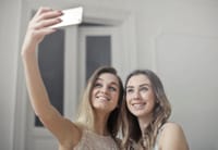 Two smiling women capturing a joyful selfie indoors, showcasing friendship and happiness.