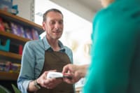 A male store clerk assisting a customer with a payment transaction in a retail shop setting.