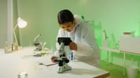 A woman scientist in a lab coat examines samples using a microscope in a laboratory setting.