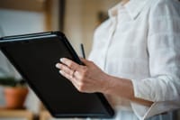 Close-up of a woman holding a digital tablet in an office environment, focusing on hand details.