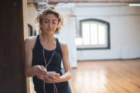 Blonde woman in a dance studio listening to music on her phone, conveying a serene and focused ambiance.