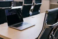 Open laptop on a wooden conference table with stylish black chairs in a modern office setting.