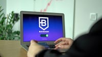 Hand holding a card near a laptop displaying blockchain connection screen.