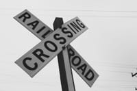 Black and white photo of a railroad crossing sign against a clear sky.