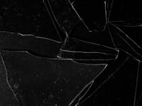 Close-up of cracked glass pieces on a black surface, emphasizing sharp edges.