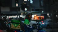Food delivery rider on motorbike at night in Bangkok, Thailand.