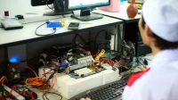 Un hombre en un uniforme de laboratorio trabajando en componentes de computadora y cableado en una estación de trabajo.