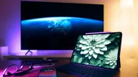 Elegante configuración de oficina en casa con dispositivos como tableta, teléfono inteligente y pantalla grande.