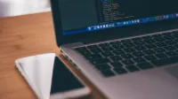 Coding setup with laptop displaying code and smartphone on a wooden table, ideal for tech themes.