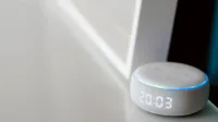Close-up of a smart speaker with a digital clock display on a minimalist surface.