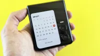 Close-up of a hand holding a flip smartphone with a calendar on screen against a vibrant yellow background.