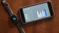 Close-up of a smartphone and smartwatch displaying a weekly report on a wooden table.