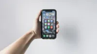 Hand holding smartphone displaying social media apps on home screen.