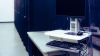 Contemporary computer with black screen placed on stand near row of server steel racks in data center