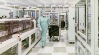 Scientist in protective gear walking in a high-tech cleanroom laboratory environment.