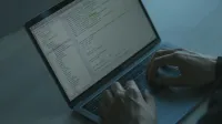 Una persona escribiendo código en una computadora portátil con un enfoque en ciberseguridad y desarrollo de software.