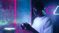 Young man focused on video gaming with vibrant neon lights illuminating the scene.