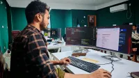 Software developer coding on dual monitors in a well-lit modern office, focused and engaged.