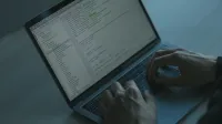 A person typing code on a laptop with a focus on cybersecurity and software development.