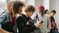 A group of diverse college students hanging out indoors and using a smartphone together.
