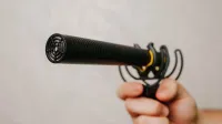 Mano sosteniendo un micrófono de escopeta con cubierta de espuma, ideal para grabación de voz y captura de audio.