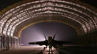 Silhouetted fighter jet in an illuminated hangar at night creates a dramatic scene.