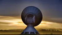 Large satellite dish silhouette against a colorful sunset, showcasing broadcasting technology.