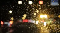 Street lights glistening through raindrops on a car window at night, creating a bright bokeh effect.