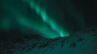 Majestic aurora borealis illuminates the night sky over snow-covered mountains.