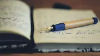 A close up of a fountain pen resting on an open notebook, highlighting handwriting and the writing process.