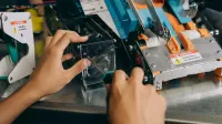 Manos de un técnico reparando maquinaria robótica con herramientas de precisión en un banco de trabajo.