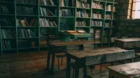 A rustic, vintage classroom featuring wooden desks and bookshelves filled with books.