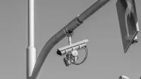 Black and white image of a surveillance camera mounted on a streetlight in an urban environment.