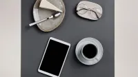 Stylish flat lay featuring coffee, cheesecake, eyeglasses, and a tablet on a gray table, perfect for lifestyle themes.