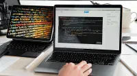 A developer writing code on a laptop, displaying programming scripts in an office environment.