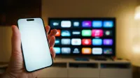 A smartphone in focus with a smart TV displaying apps in a cozy living room.
