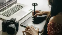 Close-up of a woman using a graphics tablet to create digital art with a laptop.
