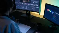 Un editor de video que usa monitores duales para editar imágenes en un estudio con poca luz.