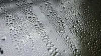 Detailed close-up of water droplets forming patterns on a black surface, showcasing texture and clarity.