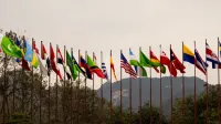 A display of various national flags on flagpoles set against a mountain backdrop, symbolizing global unity.