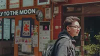 Man walking by a colorful street with shops and signs, enjoying a sunny day.