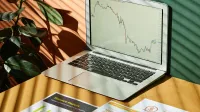 Laptop displaying a financial graph with reports, in a sunlit workspace.