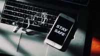 Gafas y pantalla de smartphone 'manténgase a salvo' en la computadora portátil, enfatizando el trabajo remoto.