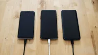 Three smartphones connected to chargers on a wooden surface, showcasing modern technology