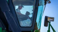 A farmer operates a harvester machine from inside the cabin on a clear day.